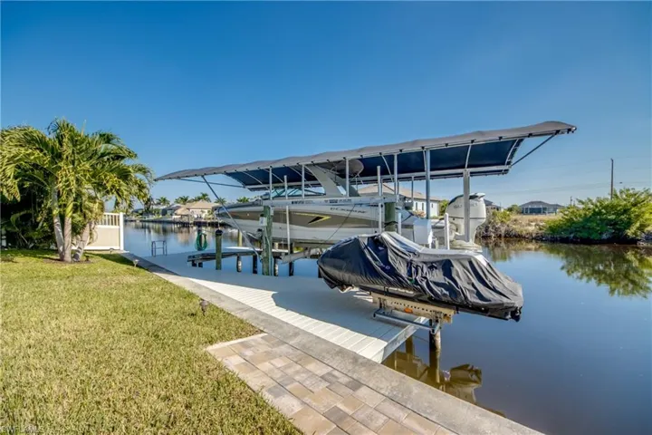 Dock area featuring boat lift, a lawn, and a water view