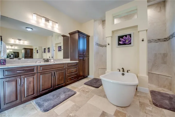 Bathroom featuring vanity, a freestanding tub, a walk in shower, and stone tile flooring