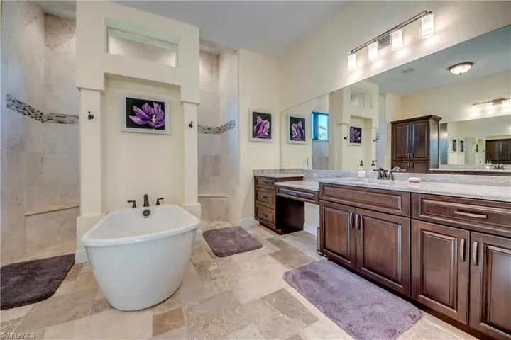 Bathroom with vanity, walk in shower, a freestanding bath, and stone tile flooring