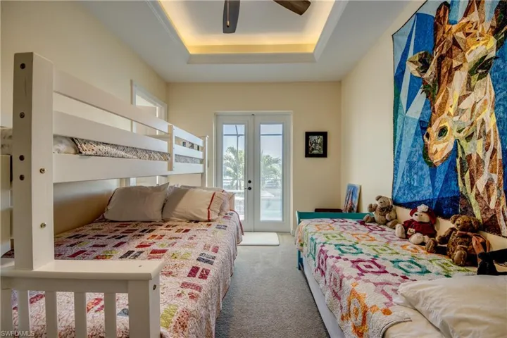 Carpeted bedroom featuring french doors, access to outside, a tray ceiling, and ceiling fan