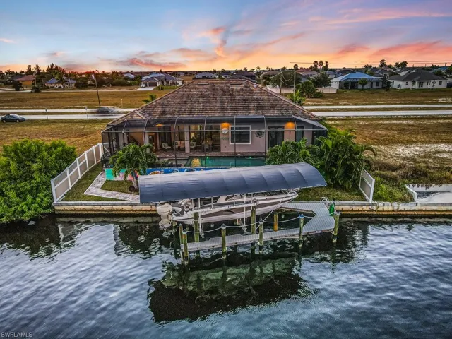 Back of house featuring glass enclosure, boat lift, a water view, and a residential view
