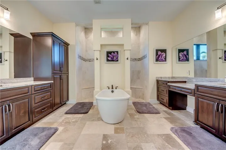 Bathroom with a freestanding bath, two vanities, a walk in shower, and stone tile floors
