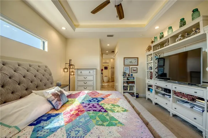 Bedroom with a raised ceiling, ensuite bath, light colored carpet, ceiling fan, and recessed lighting