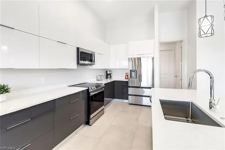 Modern kitchen featuring two-tone cabinetry, stainless steel appliances, a large single-basin sink with a gooseneck faucet, light-colored countertops, and recessed lighting