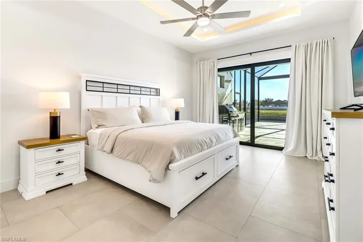 Spacious room featuring large format tile flooring, a tray ceiling with integrated lighting, a ceiling fan, and sliding glass doors opening to a screened outdoor area