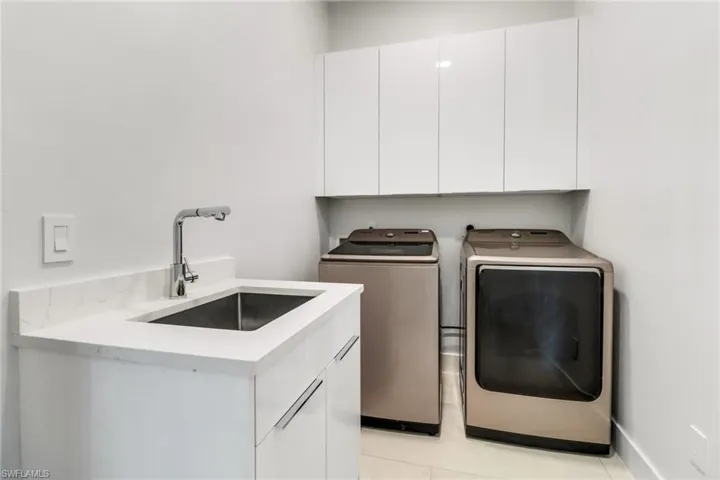 Laundry area featuring a utility sink with a chrome gooseneck faucet, white cabinetry, and a stone-finish countertop