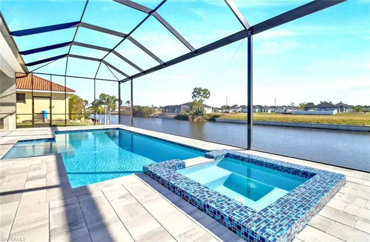Screened-in outdoor living space featuring a rectangular swimming pool, integrated spa with blue mosaic tile, and concrete paver decking