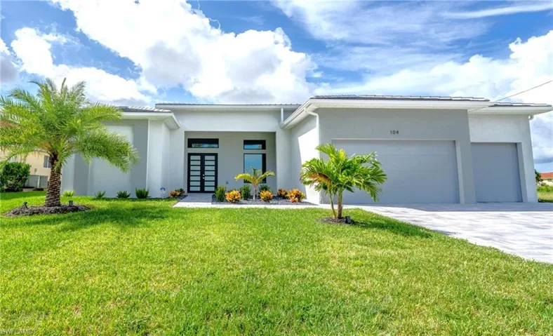 Modern exterior featuring a prominent entry with a double door, two-car garage, manicured lawn, and mature palm trees