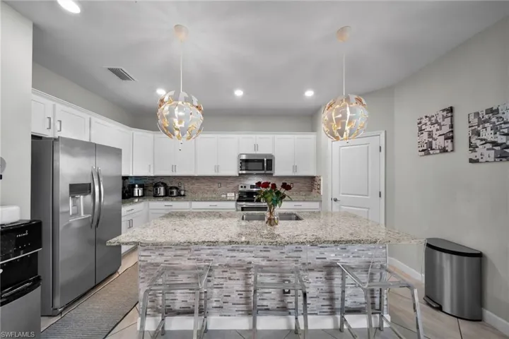 Kitchen featuring a breakfast bar area, decorative backsplash, appliances with stainless steel finishes, and an inviting chandelier