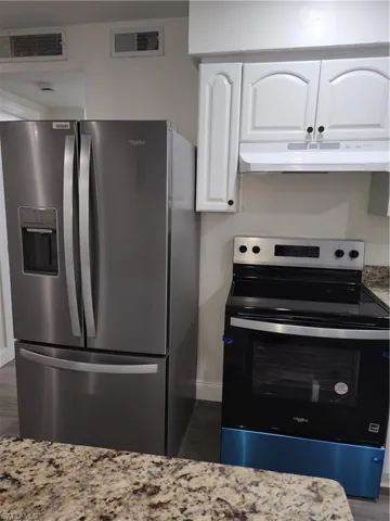 Kitchen featuring fridge with ice dispenser, range, exhaust hood, white cabinets, and light stone countertops