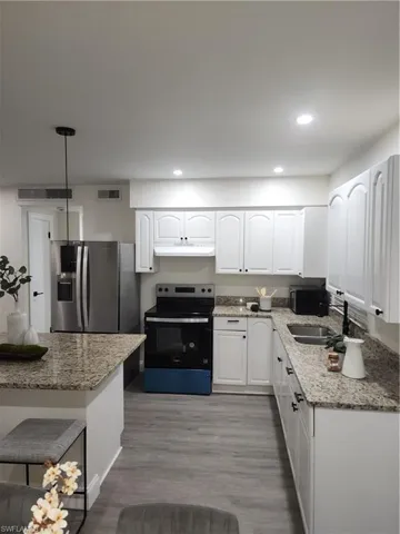 Kitchen featuring stove, fridge, exhaust hood, light stone countertops, and recessed lighting