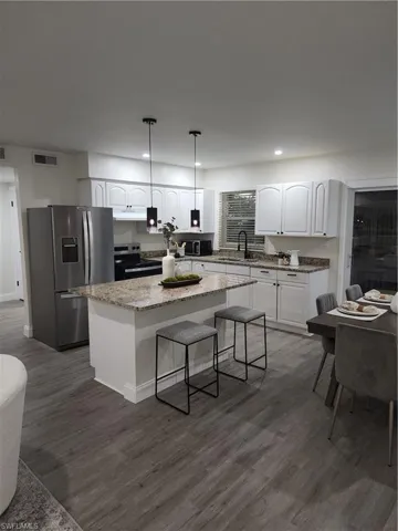 Kitchen featuring refrigerator, range, a kitchen island, white cabinetry, and dark wood-style floors