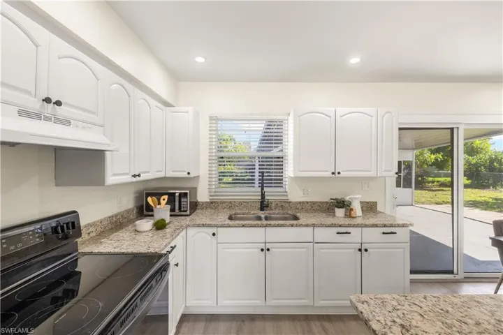 Kitchen featuring black electric range, under cabinet range hood, stainless steel microwave, light wood-type flooring, and light stone counters