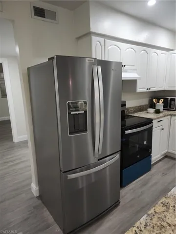 Kitchen featuring stainless steel fridge with ice dispenser, stove, ventilation hood, white cabinetry, and light wood-type flooring
