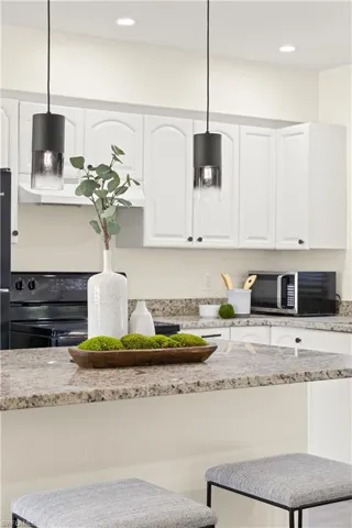 Kitchen with stainless steel microwave, electric range, white cabinetry, pendant lighting, and light stone counters