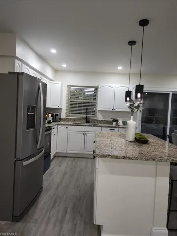 Kitchen with fridge, wood finished floors, a center island, white cabinets, and pendant lighting