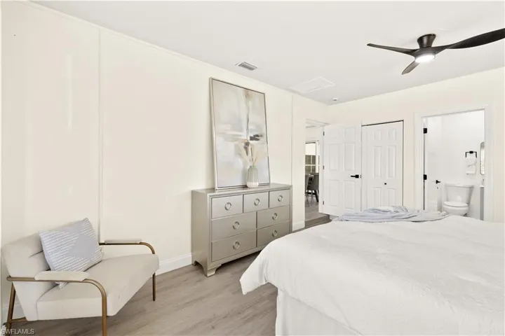 Bedroom with light wood-style flooring, ceiling fan, connected bathroom, and attic access