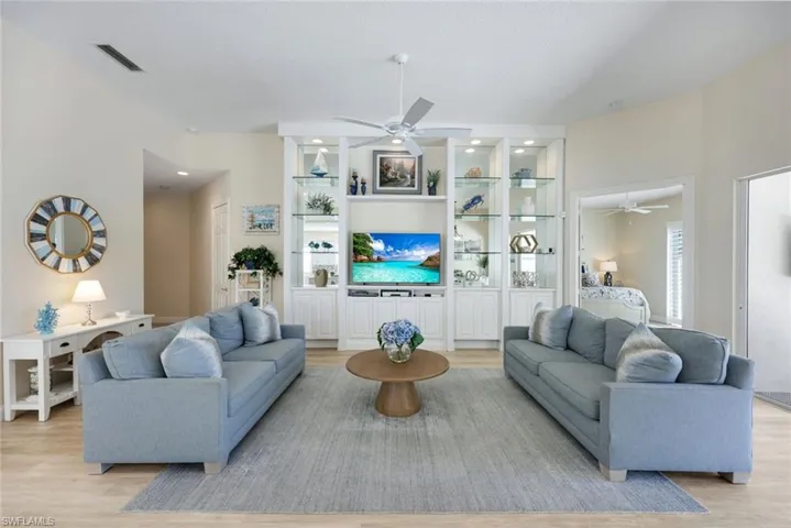 Spacious living area featuring light wood-finish flooring and a central built-in entertainment unit with integrated shelving and lighting