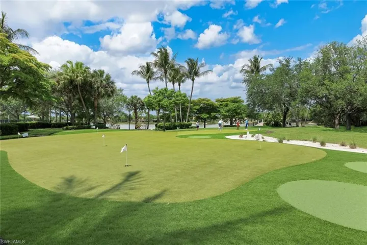 Expansive putting green with multiple holes, surrounded by lush landscaping and mature palm trees