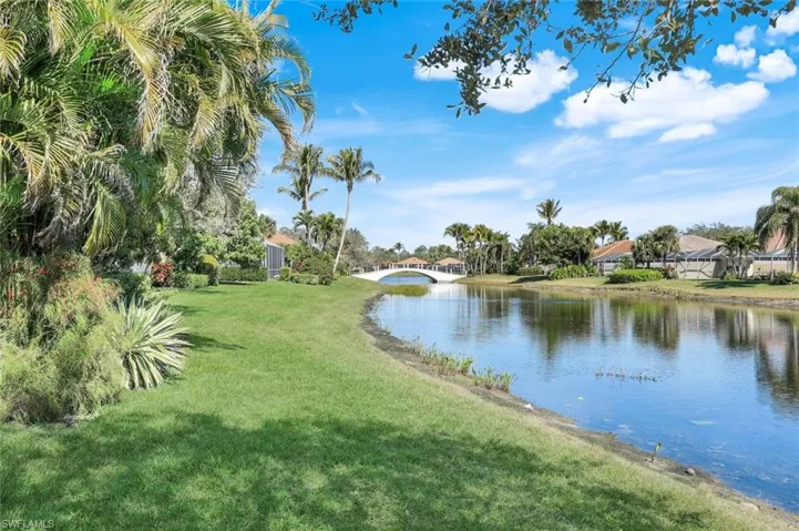 Waterfront property featuring a landscaped lawn, mature palm trees, and a decorative bridge across the water