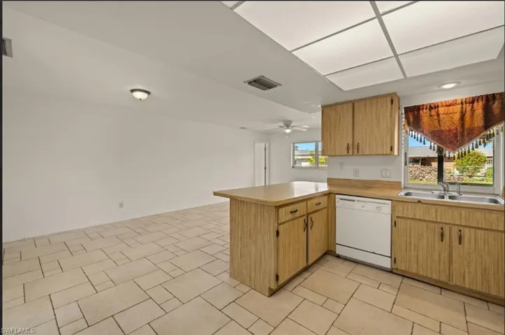 Kitchen with ceiling fan, white dishwasher, kitchen peninsula, and sink