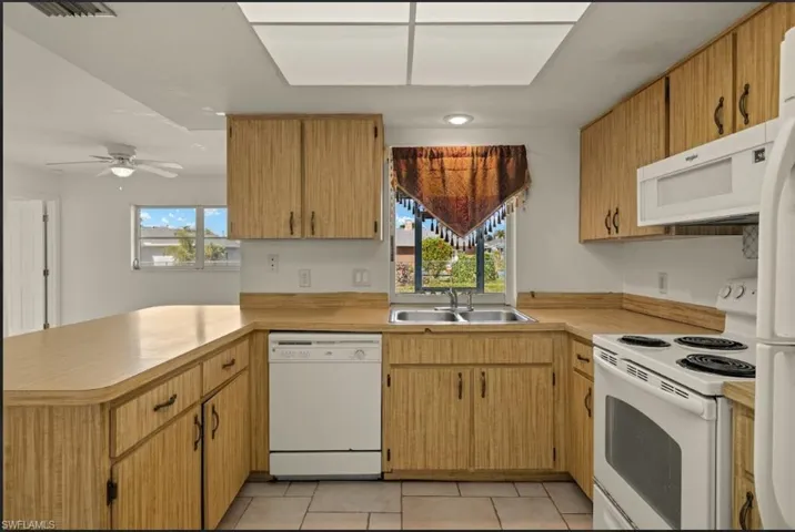 Kitchen with a healthy amount of sunlight, sink, white appliances, and kitchen peninsula