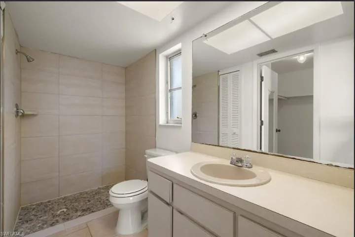 Bathroom featuring tiled shower, vanity, toilet, and tile patterned flooring