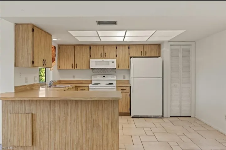 Kitchen featuring white appliances, light brown cabinetry, kitchen peninsula, and sink