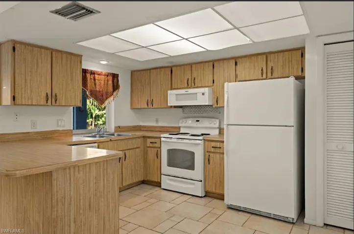 Kitchen featuring sink, white appliances, kitchen peninsula, and backsplash