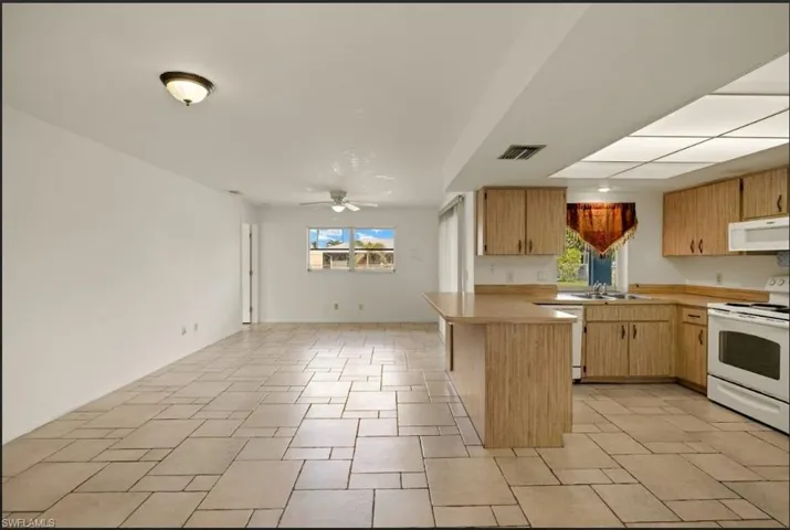 Kitchen featuring ceiling fan, sink, white appliances, and kitchen peninsula