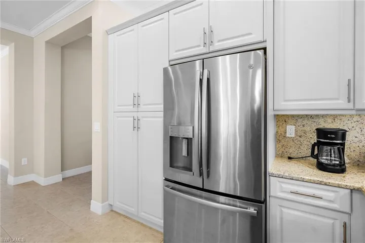 Kitchen featuring stainless steel refrigerator with ice dispenser, ornamental molding, white cabinets, light stone countertops, and light tile patterned flooring
