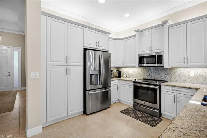 Kitchen with stainless steel appliances, decorative backsplash, light stone countertops, ornamental molding, and light tile patterned flooring