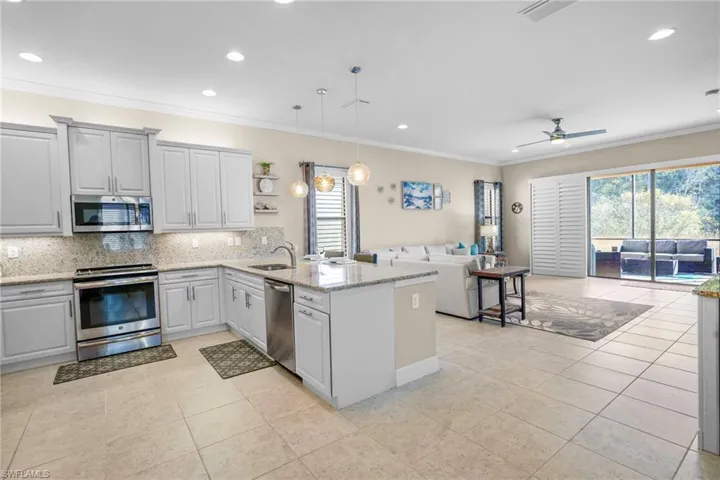 Kitchen with stainless steel appliances, light stone counters, tasteful backsplash, hanging light fixtures, and open floor plan