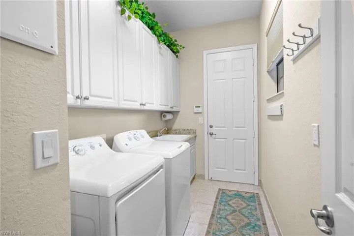 Laundry room featuring a textured wall, washer and clothes dryer, cabinet space, and light tile patterned floors