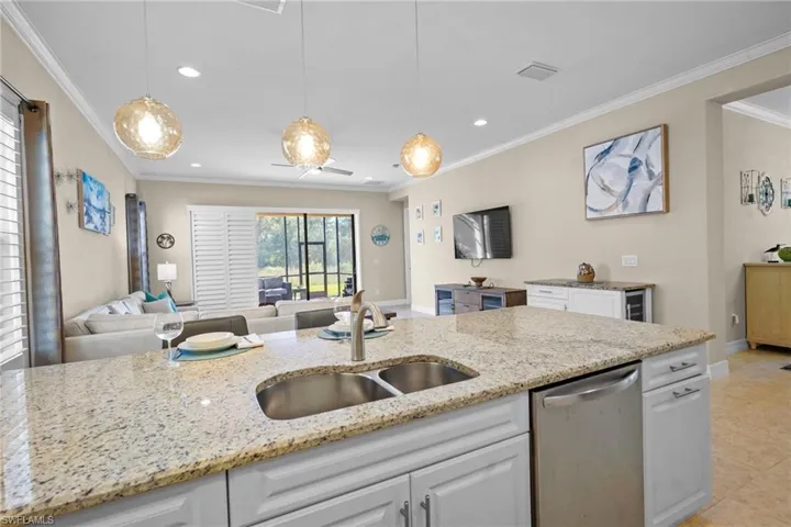 Kitchen with open floor plan, white cabinetry, dishwasher, light stone counters, and decorative light fixtures