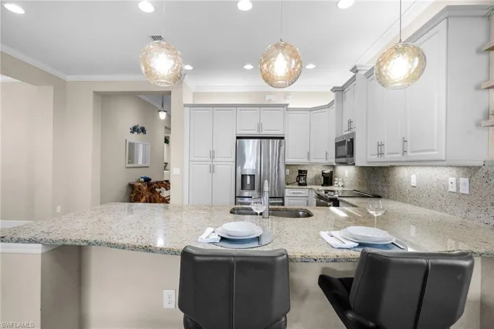 Kitchen featuring a peninsula, light stone countertops, stainless steel appliances, tasteful backsplash, and crown molding