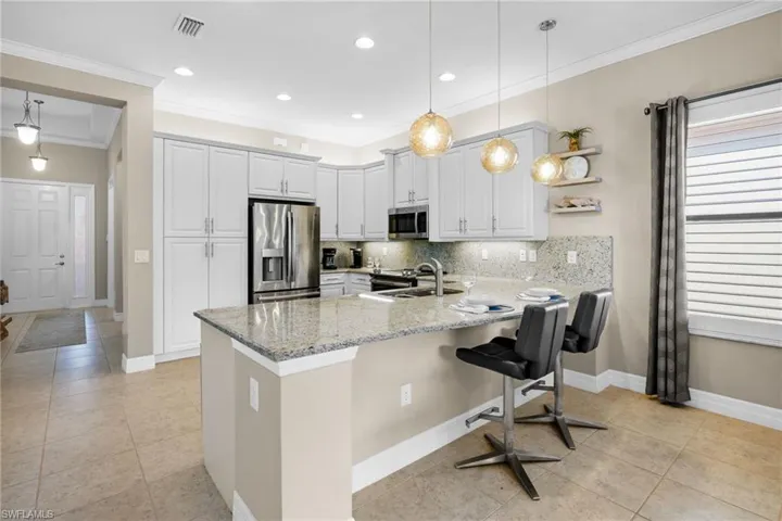 Kitchen featuring tasteful backsplash, decorative light fixtures, stainless steel appliances, light stone counters, and a peninsula