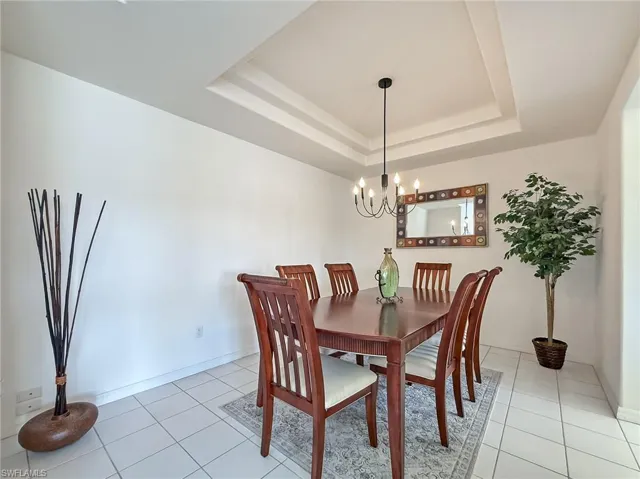 Dining area featuring light tile patterned floors, a tray ceiling, baseboards, and a chandelier