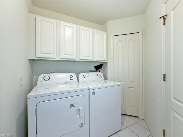 Clothes washing area with light tile patterned floors, cabinet space, baseboards, and washer and clothes dryer