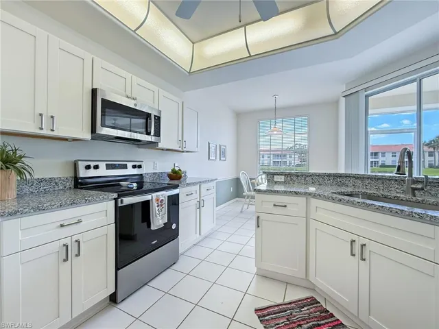 Kitchen with stainless steel appliances, white cabinetry, a sink, light stone counters, and light tile patterned floors