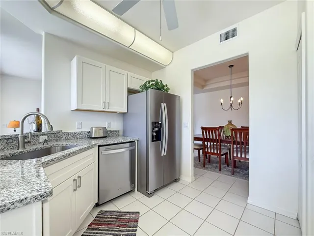 Kitchen with visible vents, stainless steel appliances, a sink, ceiling fan with notable chandelier, and light stone counters