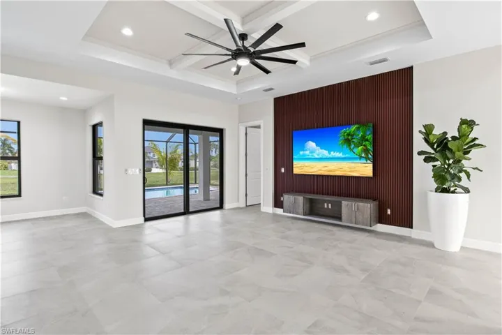Unfurnished living room featuring ceiling fan, a raised ceiling, coffered ceiling, and light tile patterned floors