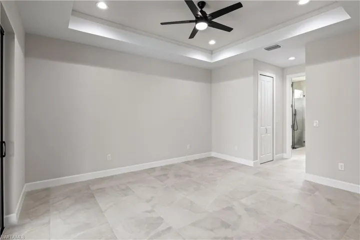 Tiled empty room featuring ceiling fan and a raised ceiling