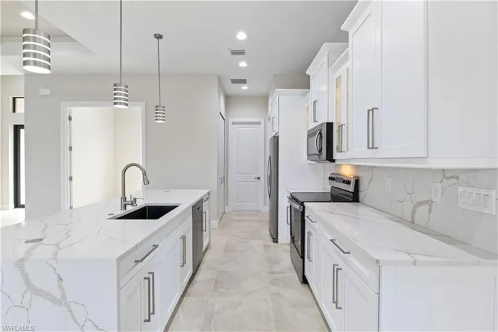 Kitchen with decorative light fixtures, light stone countertops, light tile patterned floors, and stainless steel appliances