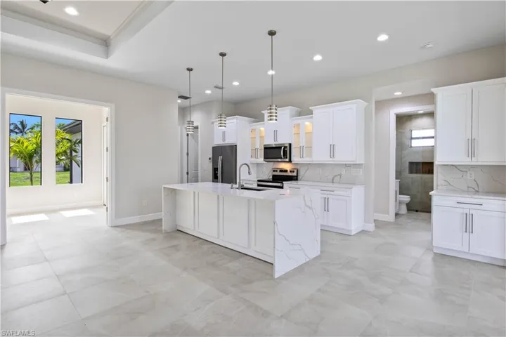 Kitchen with appliances with stainless steel finishes, a center island with sink, light tile patterned floors, light stone countertops, and white cabinetry