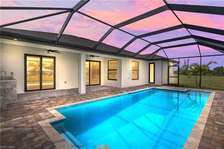 Pool at dusk with a patio, ceiling fan, and glass enclosure