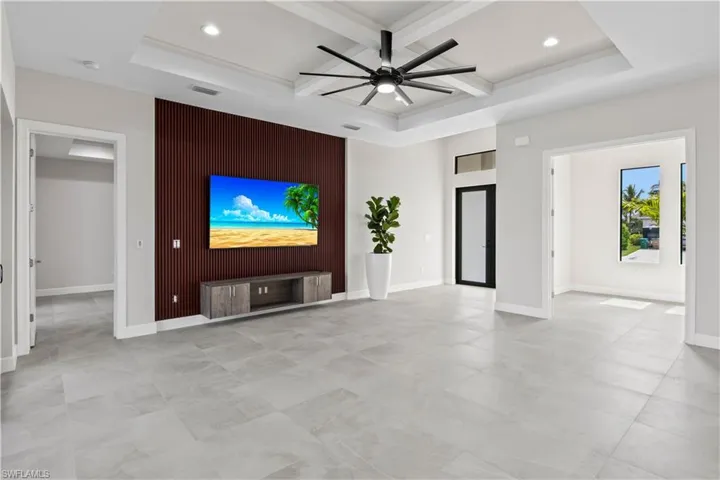 Unfurnished living room featuring beamed ceiling, light tile patterned floors, ceiling fan, and a tray ceiling
