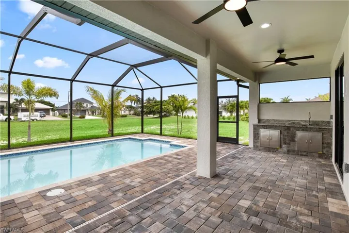 View of swimming pool featuring a patio area, ceiling fan, a lawn, and glass enclosure