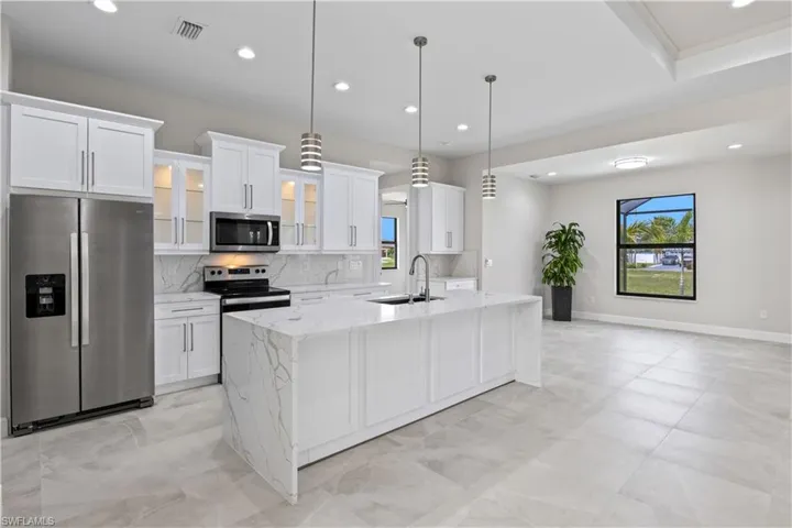 Kitchen with stainless steel appliances, decorative backsplash, white cabinets, sink, and light stone counters