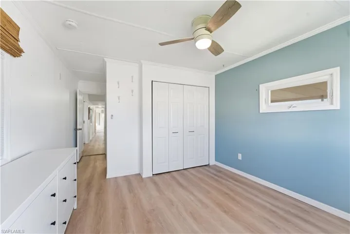 Unfurnished bedroom with a closet, light wood finished floors, ornamental molding, and a ceiling fan